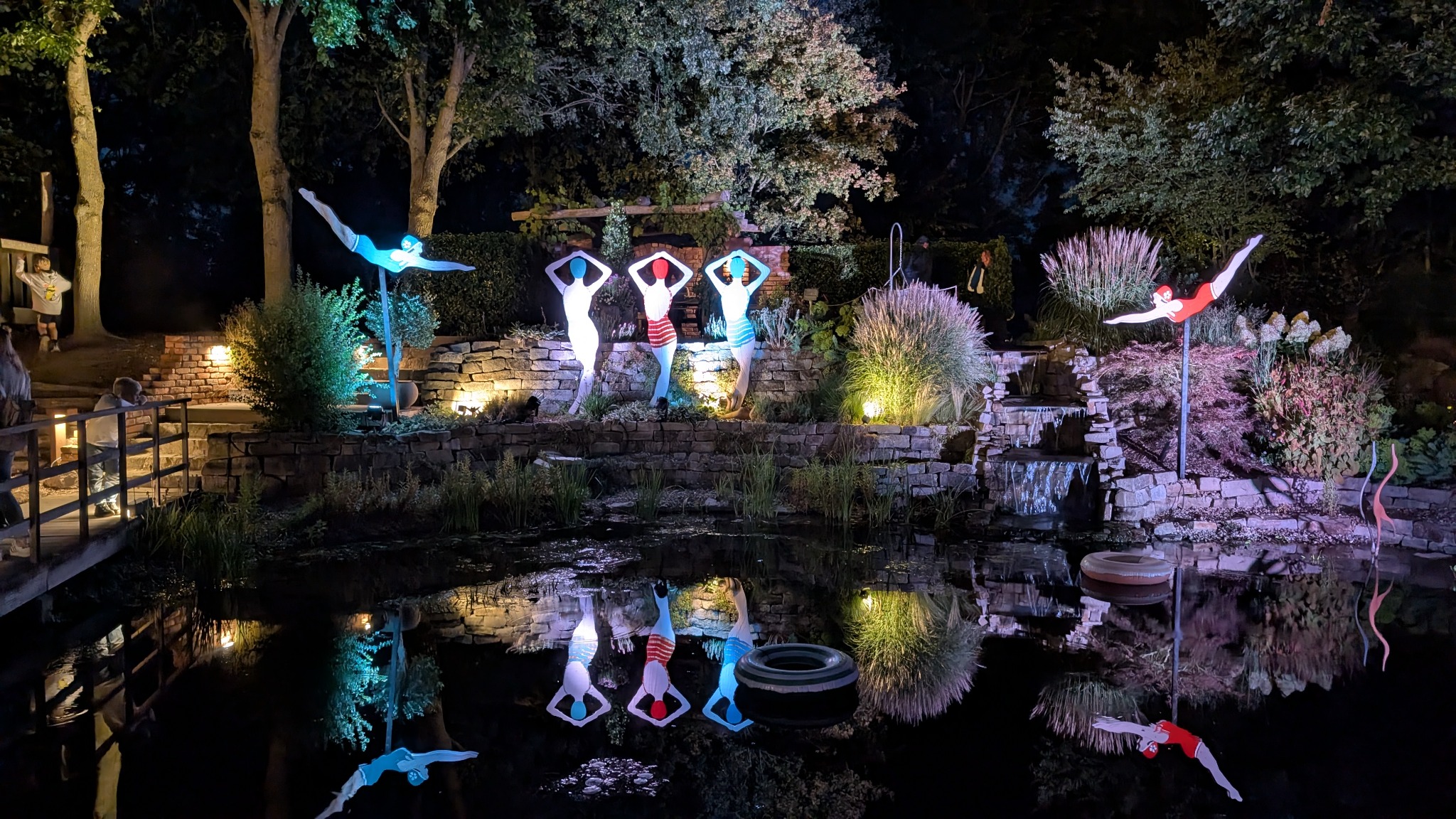 Beleuchtete Figuren und Pflanzen spiegeln sich in einem Gartenteich